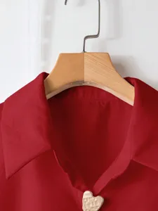 Primo piano di un colletto rosso tinta unita con un esclusivo bottone metallico a forma di cuore.
