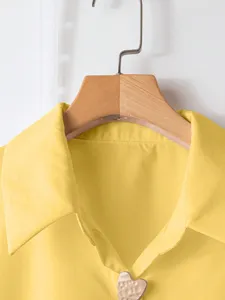 Vista dettagliata della camicia casual gialla retrò con un chic bottone a cuore.