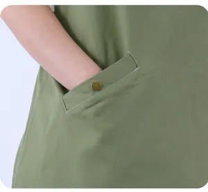 Detail view of green cotton work apron pocket with metal snap button and neat stitching.