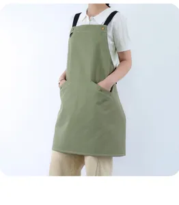 Detail view of green cotton work apron with black straps and metal rivets for kitchen use.
