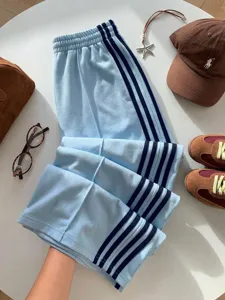Detailed view of light blue casual track pants with retro side stripes and elastic high waist.
