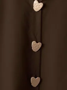 Primo piano dettagliato di una camicia marrone con bottoni metallici a cuore testurizzati.