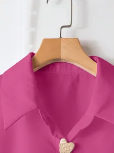 Dettaglio in primo piano del colletto della camicia rosa da donna con bottone a cuore.