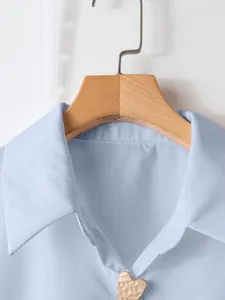 Primo piano del colletto della camicia azzurra e dell'esclusivo bottone in metallo a cuore.