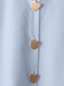 Primo piano dettagliato di una camicia casual azzurra con bottoni metallici dorati a cuore.