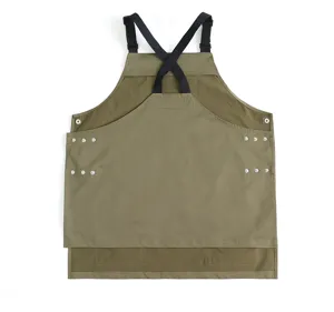 Detail view of a durable green work apron with black cross-back straps and rivet accents.