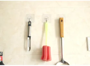 Detail shot of transparent traceless wall hooks hanging kitchen utensils on tiled wall.