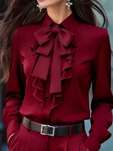 Elegante blusa burdeos de manga larga con cuello solapa, gran lazo y elegante botonadura de volantes.