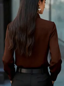 Detalle de blusa marrón elegante de manga larga, cuello clásico y corte ajustado y entallado.