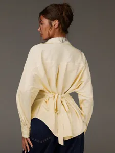 Dettaglio posteriore di una camicia a maniche lunghe a righe gialle con cintura annodata in vita.