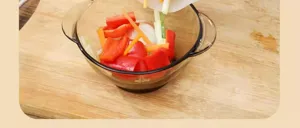 Kitchen detail shot showing a glass preparation bowl with fresh vegetables on a wooden board.