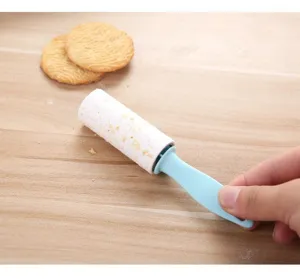 Compact sticky lint roller detail shot showing dust and crumb removal on a wooden surface.