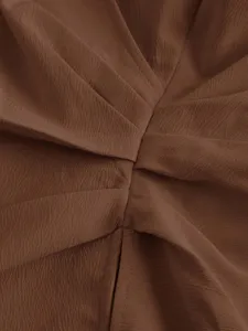 Detailed shot of brown textured fabric with elegant crossover pleating design for women shirt.