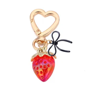 Joli porte-clés fraise avec fermoir cœur et nœud noir, détails strass brillants.