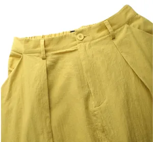 Detail shot of women high waist yellow pleated A-line skirt waistband with button and belt loops.