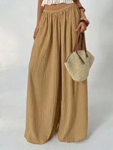 Detailed view of pleated wide-leg trousers, elastic high waist drape design in classic khaki.
