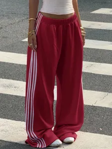 Close-up detail of red wide-leg sweatpants featuring classic white side stripe design.
