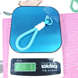 Blue woven mobile phone lanyard strap with white wrap detail and clear hanging tab on scale.