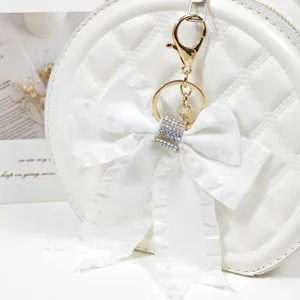 White quilted round bag with rhinestone bow keychain detailed charm accessory for women.