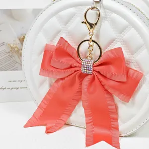 Red ribbon bow bag charm keychain with sparkling rhinestone ring, elegant gold metal clasp.
