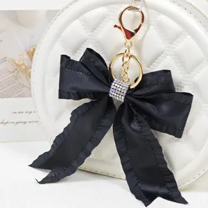 Detailed view of black pleated ribbon bow keychain with rhinestone charm and gold hardware.