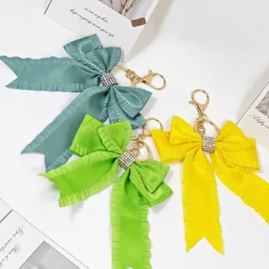 Bowknot bag charm keychain set featuring pleated ribbon, rhinestone ring, and gold hardware.