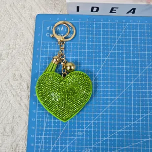 Vue détaillée du porte-clés cœur en strass vert avec pompon et accessoire doré chic.