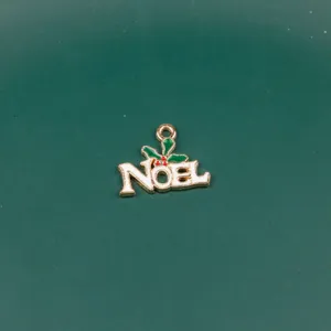 Close-up detail of a gold-tone metal NOEL Christmas charm pendant with green leaves and red berries.