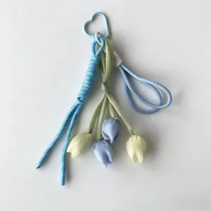Detail shot of handmade ribbon tulip flower keychain with heart clasp and braided cords for bags.