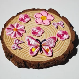 Primo piano di toppe ricamate con farfalle e fiori rosa su legno, perfette per lavori fai da te.