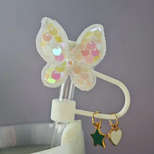 Primo piano dettagliato di un simpatico copricanna di paglia a farfalla con ciondoli stella e cuore.