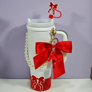 Vue détaillée du gobelet Stanley blanc avec nœud papillon rouge, chaîne de perles et accessoire.