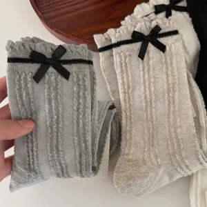 Close-up detail of cute ribbed mid-calf socks featuring a sweet black bow and knit vertical stripes.