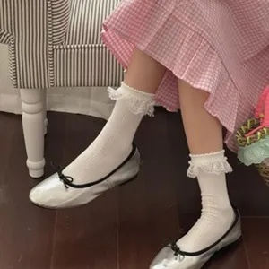 Detailed view of women's white ruffle lace mid-calf socks paired with silver ballet flats.