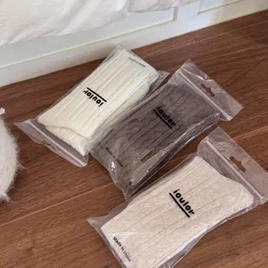 Detailed shot of cable knit over-the-knee socks in white, brown, and beige, neatly packaged.