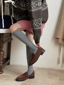 Detail shot showcasing grey calf socks paired with brown loafers and knit sweater in a cozy room.