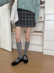 Detail shot showing grey knit calf socks styled with a chic cardigan and plaid skirt.