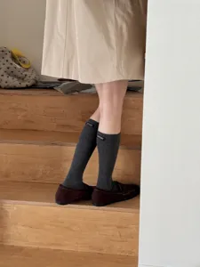 Detail view of dark grey calf socks with woven label, styled with loafers and skirt.