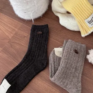 Close-up detail of cozy wool knit socks in black and brown with button decor and tags.