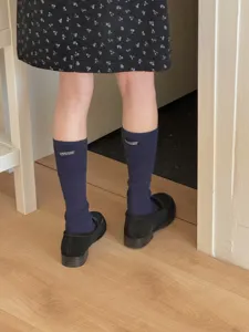 Detailed shot of dark blue cotton slouch calf socks with letter label worn with shoes.