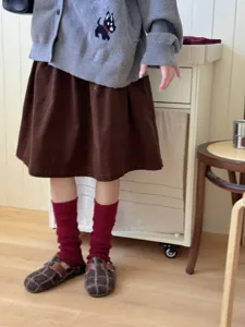 Detailed view of dark red knitted leg warmers with cable pattern, worn with skirt in room.