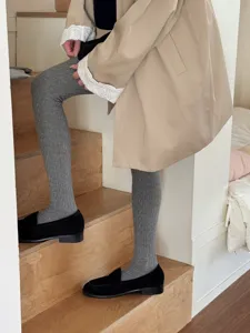 Detail shot of solid color cable knit tights worn on stairs, soft and elastic ribbed leggings.