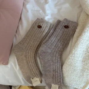 Close-up detail shot of cozy ribbed wool socks featuring cute decorative buttons and tag.