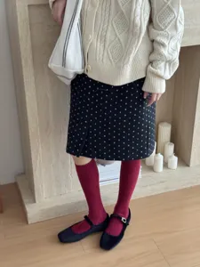 Detail shot of solid color red knee high socks styled with a cozy knit cardigan and skirt.