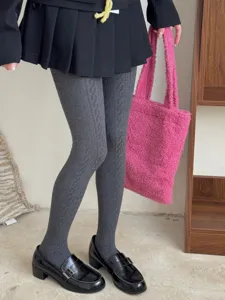 Detailed shot of solid color cable-knit tights styled with a skirt and loafers for women.