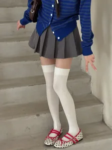 Detail shot of white over-the-knee socks paired with grey pleated skirt and college style shoes.