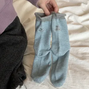 Primo piano dettagliato di calzini in maglia azzurra con risvolti grigi e delicato ricamo.
