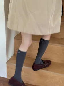 Close-up detail of grey mid-calf socks with small woven label worn on wooden stairs.