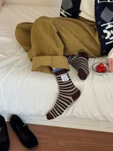 Cute striped mid-calf socks with adorable puppy patch detail, worn on cozy bed background.