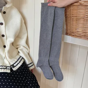 Detail shot of grey over-the-knee knit socks shown against a cozy home background.